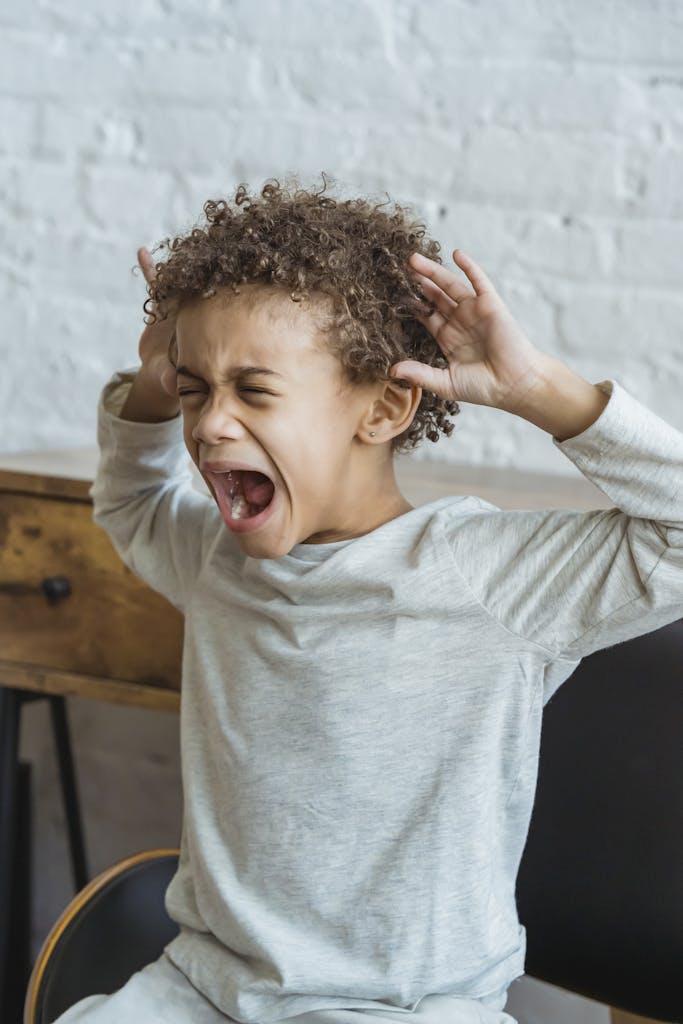 Young black child showing frustration in an indoor setting, hands on head in distress.