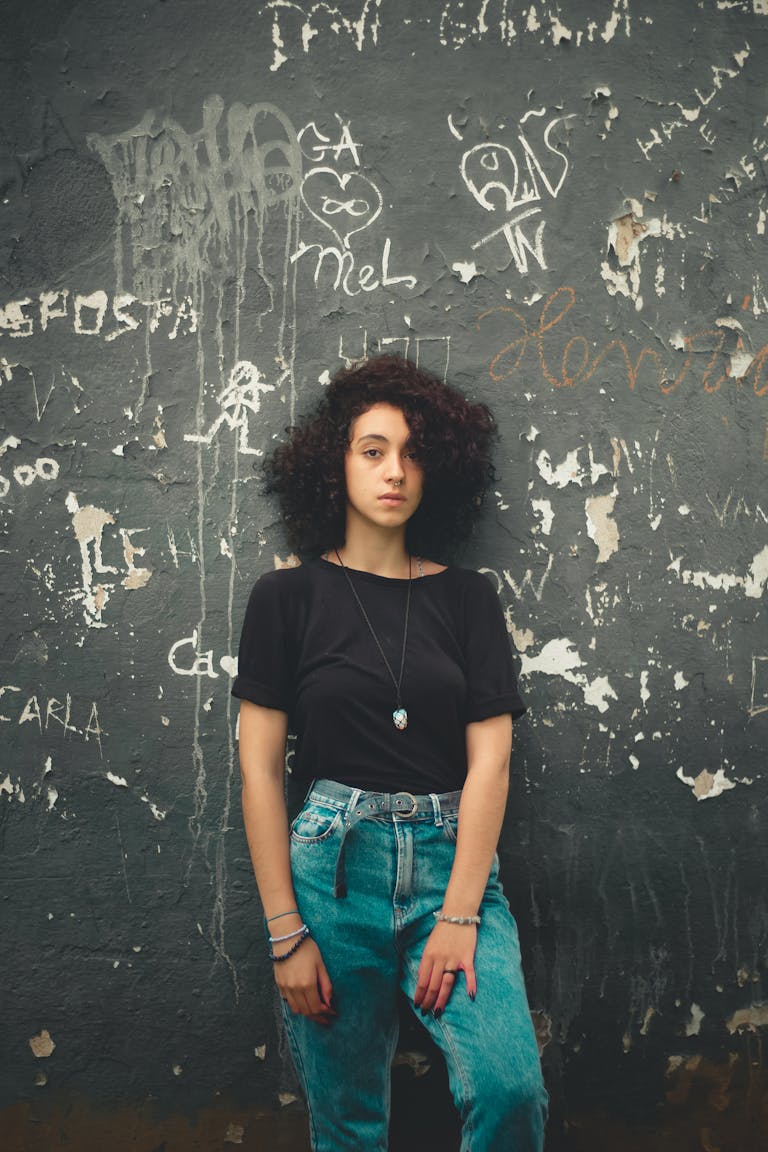 Young woman posing confidently against a graffiti-covered wall in urban setting.